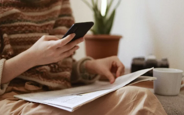 Reader checking news on a smartphone next to a newspaper, the audience a Search Profile badge or Preferred Sources button reaches